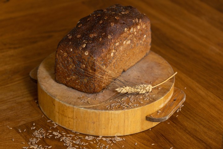 Loaf of bread with seeds on a wooden board with a grain stalk.