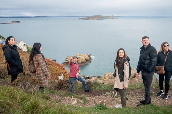 Group of people on a grassy cliff overlooking the sea and an island.