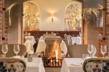 Elegant restaurant with ornate chairs, set tables, and a warm fireplace.