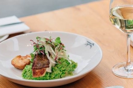 Gourmet dish with fish, pea puree, and garnish on a plate next to a glass of white wine.