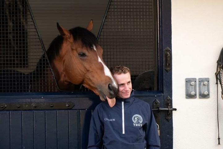 Brown horse nuzzles a person standing by a stable door.