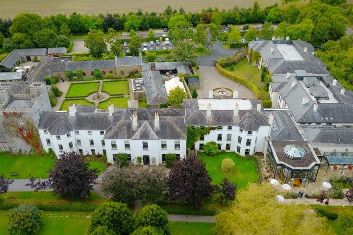 Aerial view of a large estate with a castle, gardens, and adjacent modern buildings.