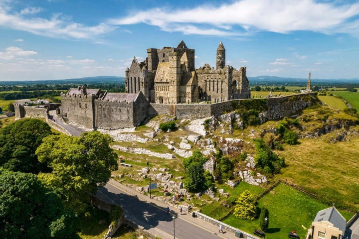Medieval castle ruins on a hill surrounded by green fields and trees.