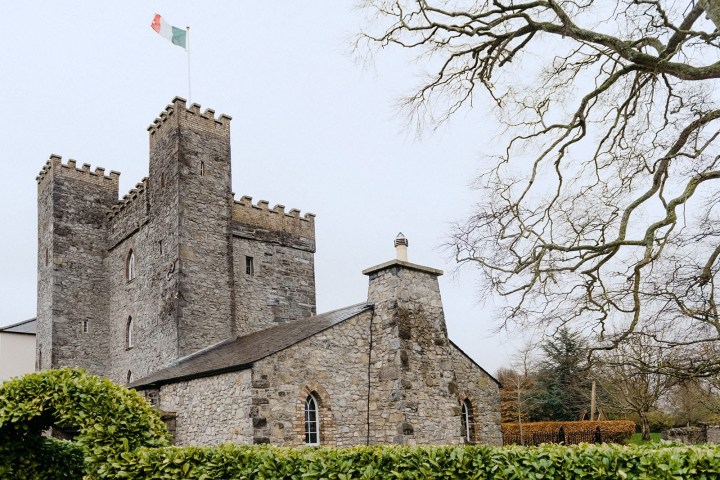 Stone castle with battlements and flag, surrounded by trees and bushes.