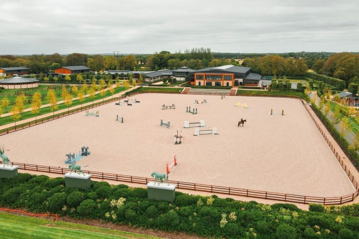 Aerial view of an equestrian arena with horse jumps, surrounded by green landscape.