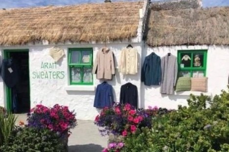 Thatched cottage with sweaters hanging outside, surrounded by flowers.