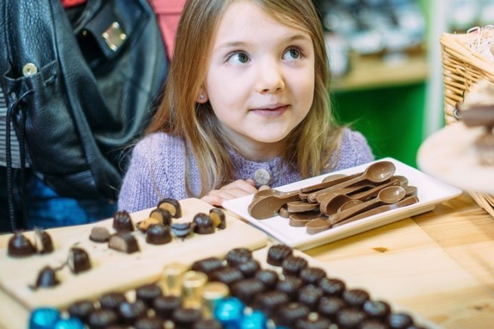 Young girl looking at chocolate pieces and chocolate spoons on a table.