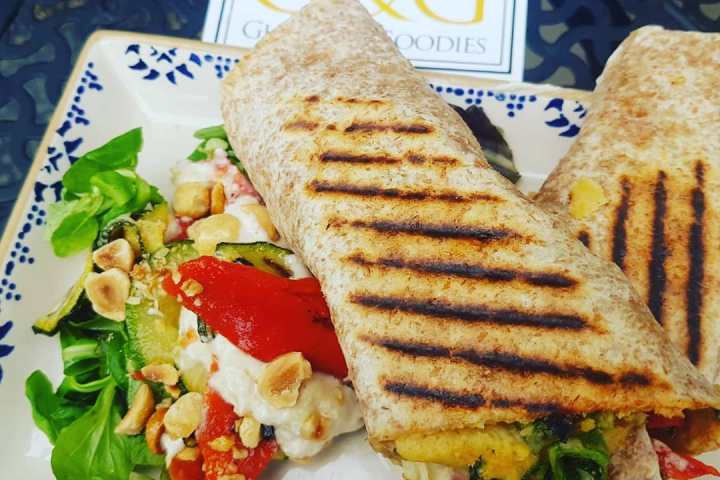 Grilled wraps on a plate with mixed greens, nuts, and roasted vegetables, label in background.