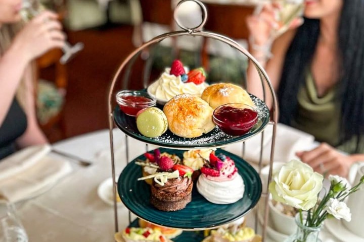 Two women enjoying tea with a three-tier tray of assorted pastries and sandwiches.