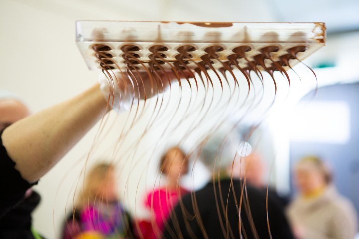 Chocolate drips from mold held in hand, with blurred people in background.