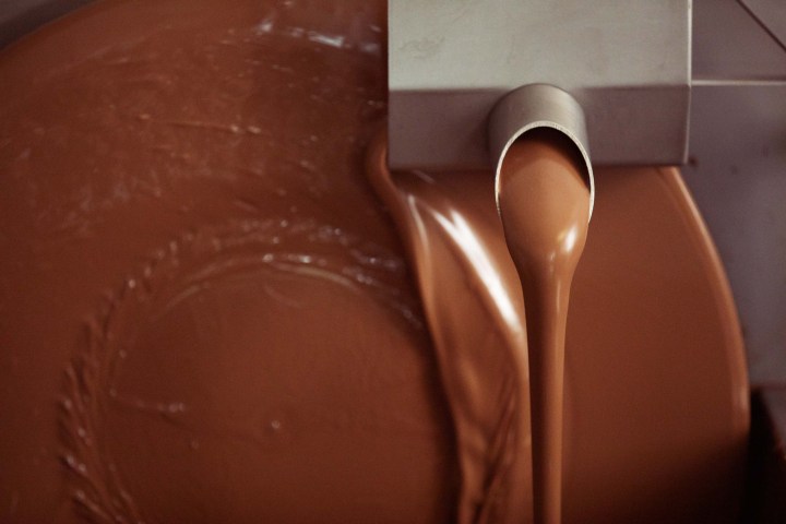 Flowing melted chocolate from a stainless steel spout into a container.