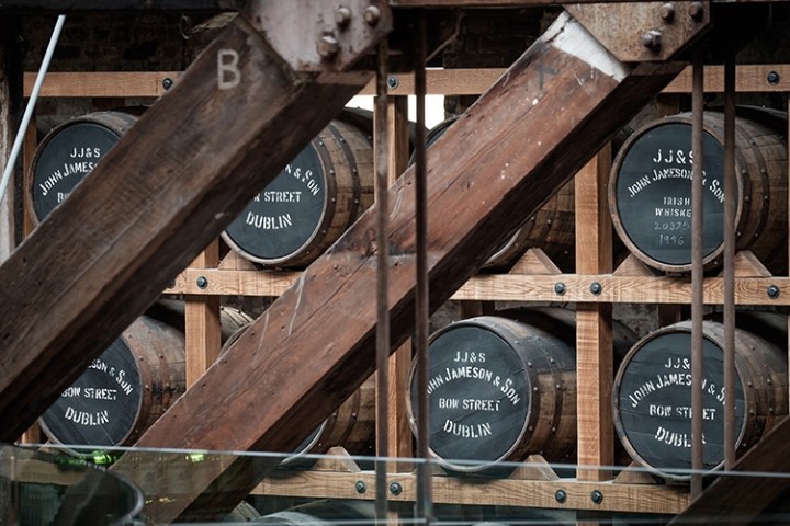 Aged whiskey barrels stacked in a wooden rack at a distillery.