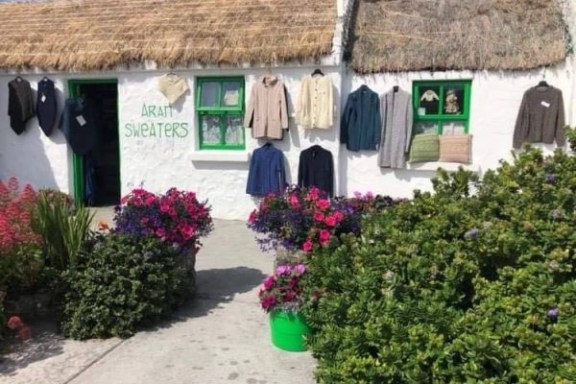 Small shop with thatched roof displaying sweaters and surrounded by colorful flowers.