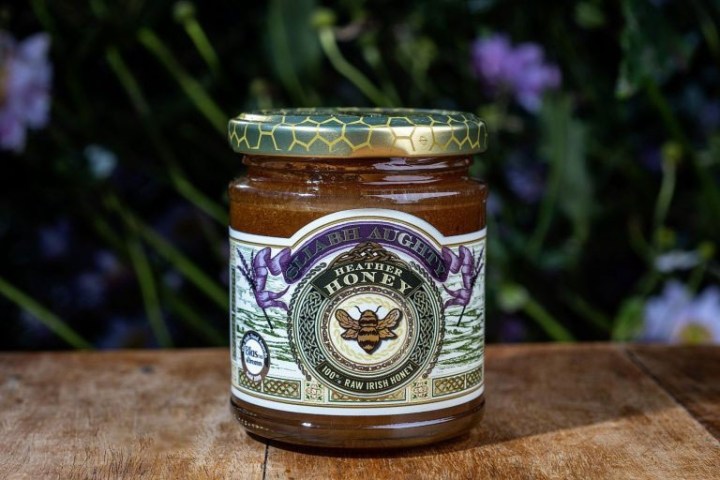 Jar of raw Irish heather honey on a wooden surface.