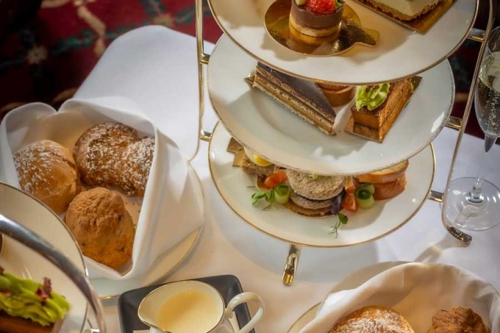 Three-tiered stand with assorted pastries and sandwiches with scones and cream on the side.