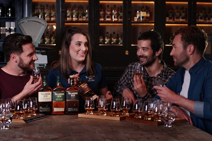 Four people enjoying a whiskey tasting with bottles and glasses on a wooden table.