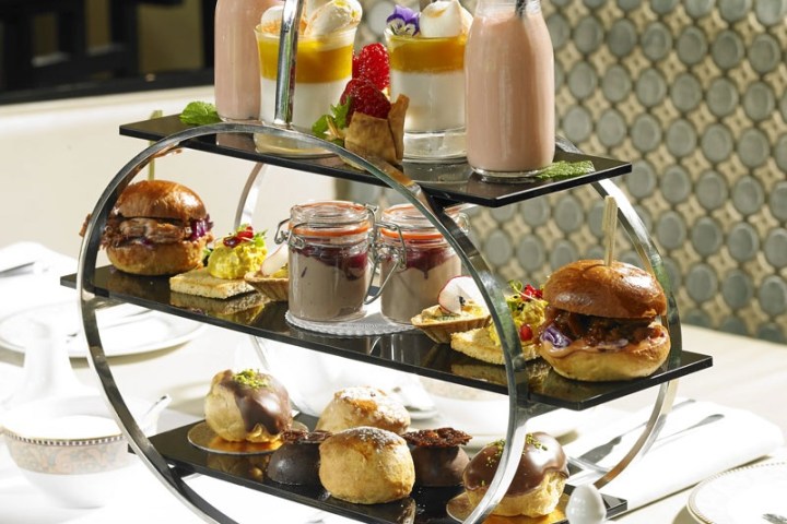 Three-tiered stand with afternoon tea pastries and drinks on a table.