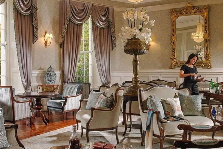 Elegant living room with chandelier, mirrored wall, and a person serving drinks.