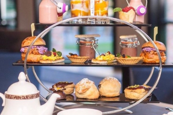 Elegant afternoon tea setup with tiered platter, sandwiches, pastries, and tea set on a table.