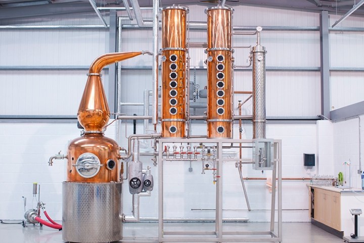 Copper distillery equipment with tall columns in a modern industrial setting.