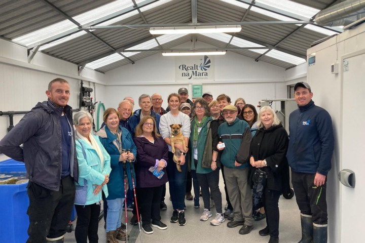 Group of people posing indoors under a metal roof with signage above.