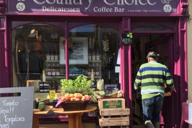 A delicatessen storefront with fresh produce and a person entering.