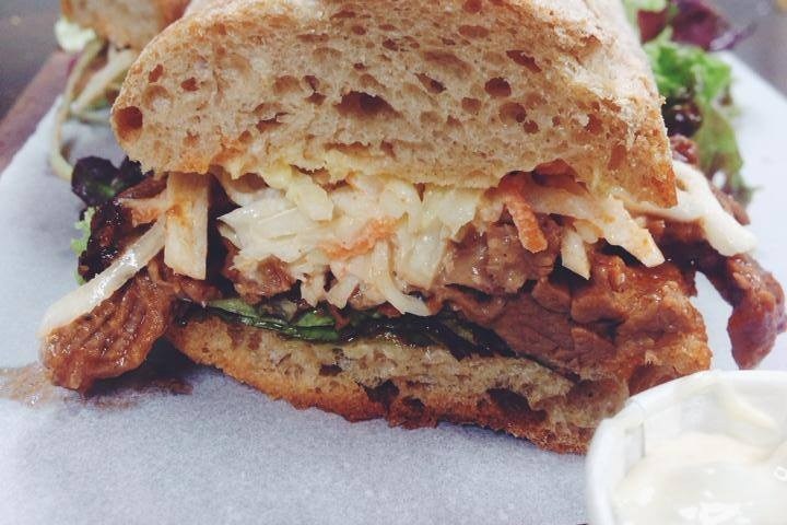 Close-up of a sandwich with meat and coleslaw on a wooden board, mayonnaise cup on the side.