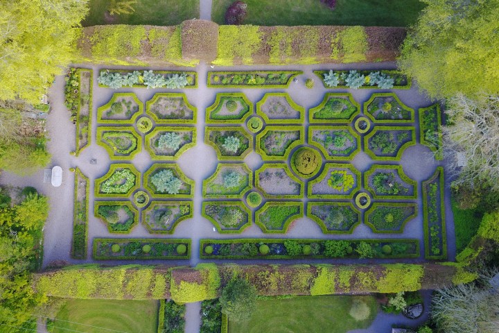 Symmetrical garden with geometric hedges and gravel paths viewed from above.