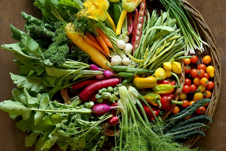 Variety of fresh colorful vegetables arranged in a wicker basket on a wooden surface.