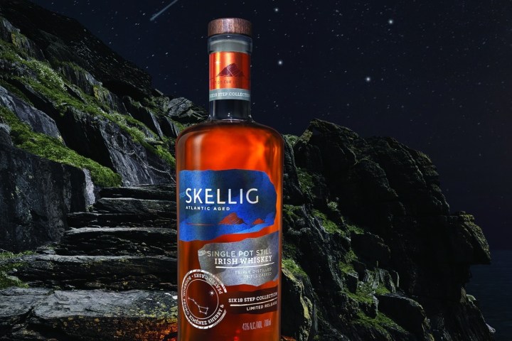 Bottle of Skellig whiskey on rocky path under starry night sky.