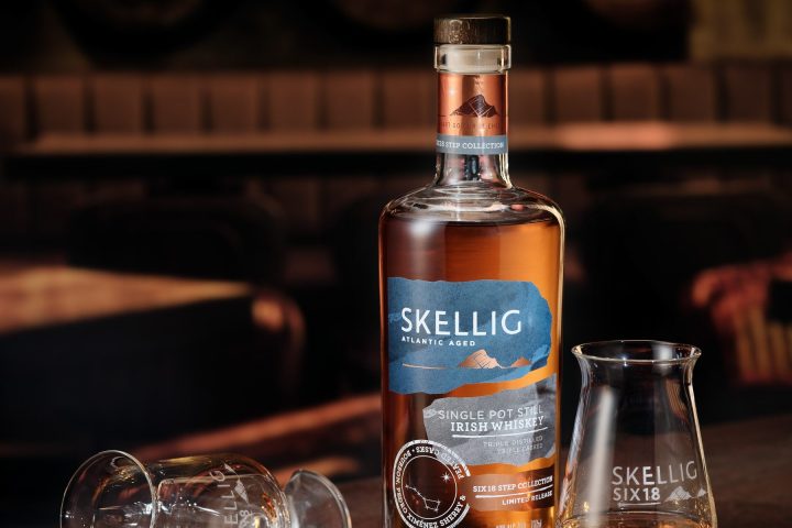 Bottle of Skellig whiskey with two glasses, one tipped over, on a dark wooden table.