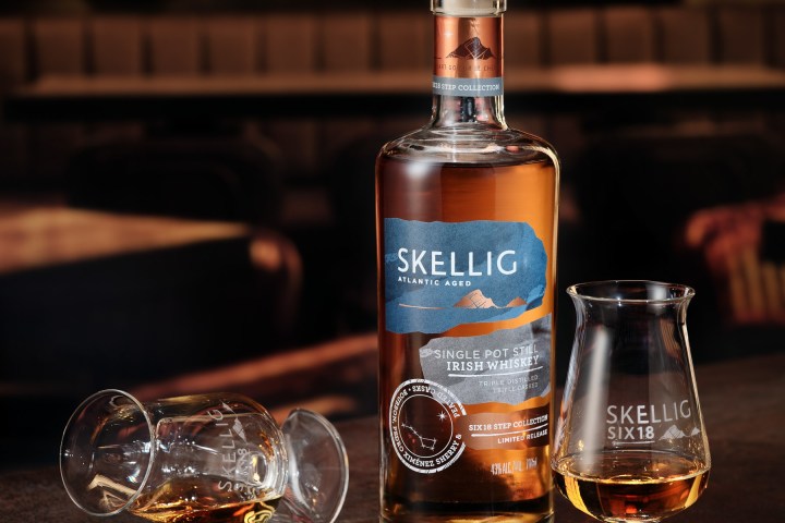 Bottle of Skellig whiskey with two glasses on a dimly lit bar counter.