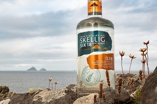 Gin bottle on rocky cliff with distant islands and cloudy sky background.