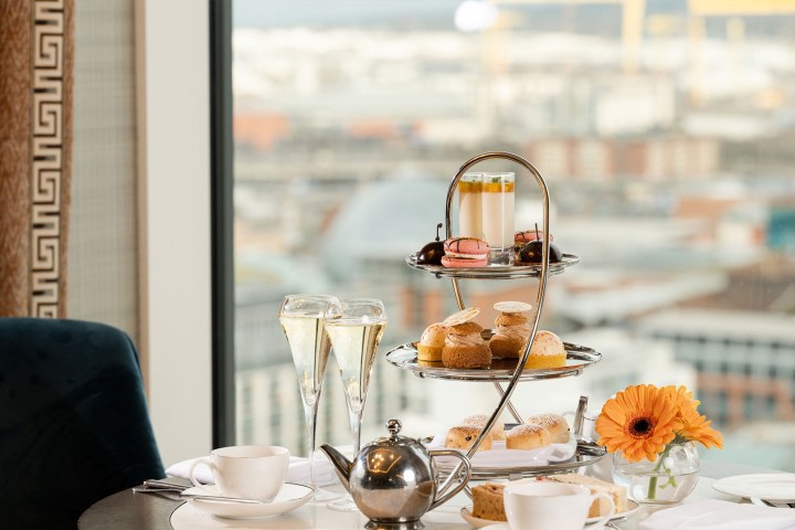Afternoon tea setup with pastries, tea set, two champagne glasses, and a city view.