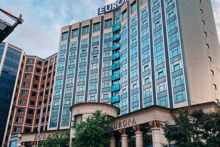 Tall building with large 'Europa' sign and columns, street view with cars and trees.