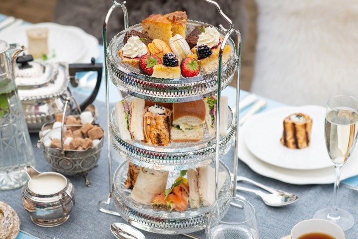 Three-tiered stand with desserts and sandwiches on a table set for tea.