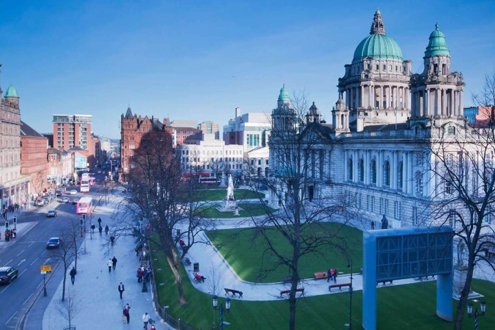 Busy city street and park with historic building and blue sky.