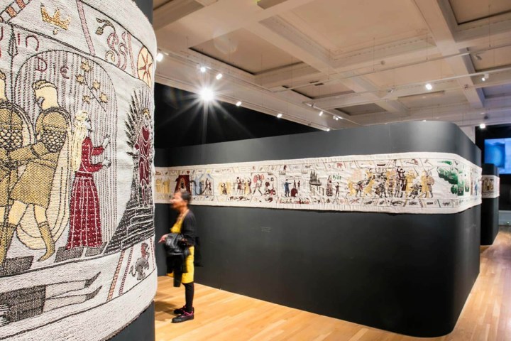 Exhibit of an embroidered tapestry in a museum with a visitor observing.
