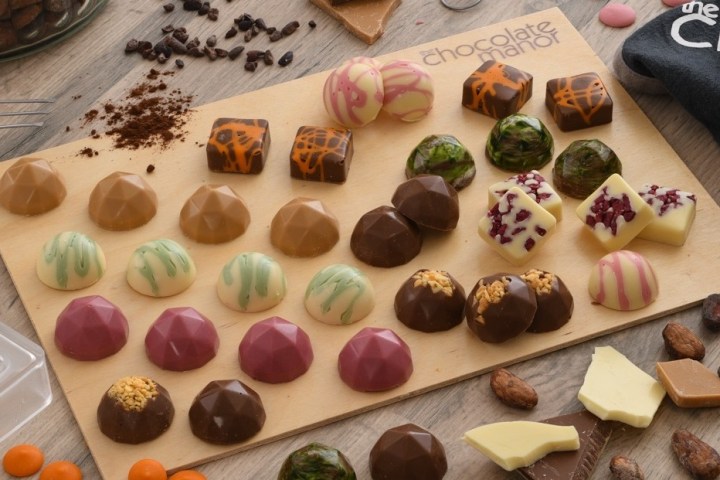 Assorted artisan chocolates on a wooden board with cacao beans scattered around.