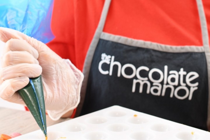 Person in apron piping yellow chocolate into molds on a table.