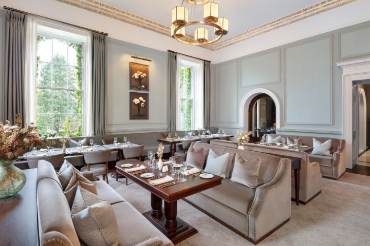 Elegant dining room with gray sofas, tables set with dishes, large windows, and a chandelier.