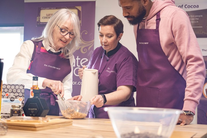 Three people in aprons preparing ingredients at a cooking class.