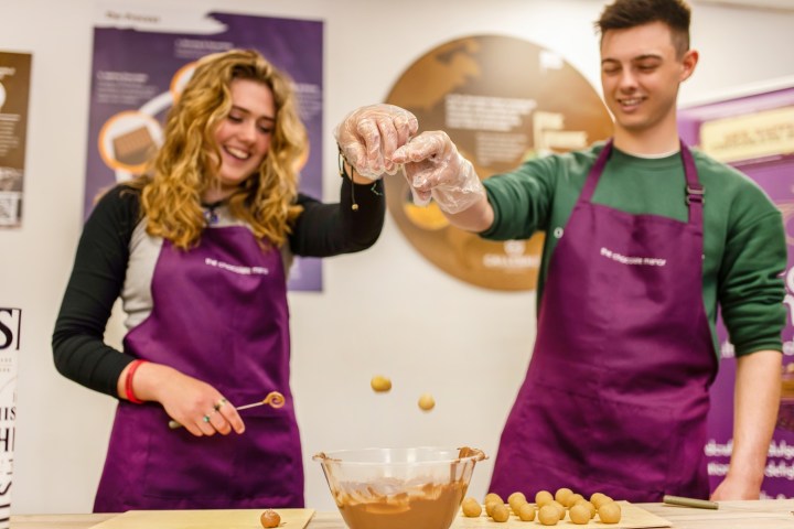 Two people in purple aprons making chocolate treats, using bowls and utensils on a table.