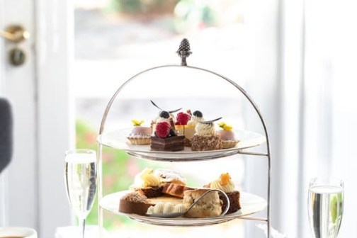 Three-tiered cake stand with pastries on a table set for afternoon tea.