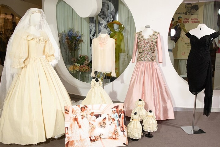 Exhibit of vintage dresses, including a wedding gown and colorful dresses, with a photo display in a fashion museum.