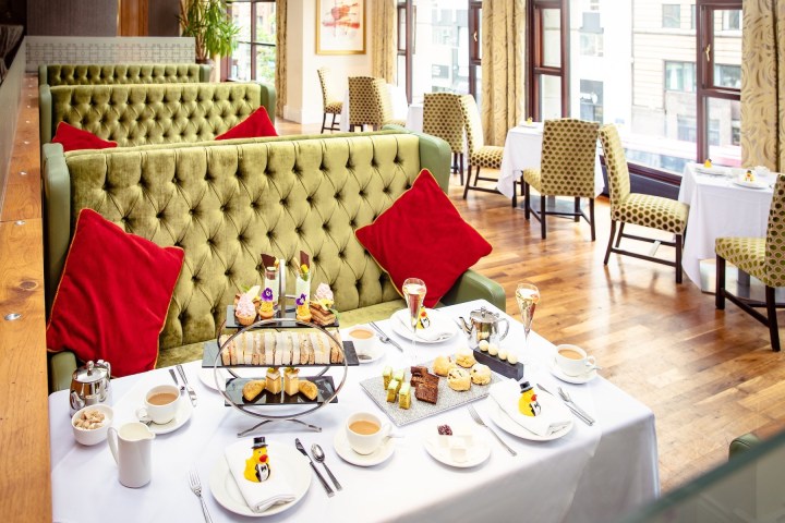 Luxurious afternoon tea set on a table in a plush dining area with green velvet booths and red pillows.