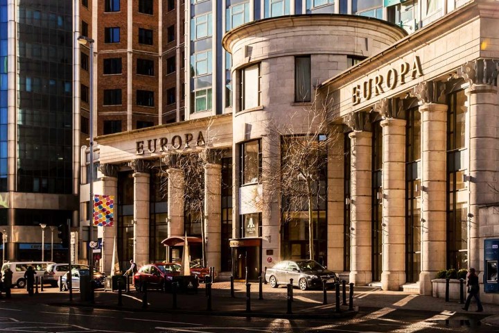 Sunlit entrance of Europa building with columns and parked cars.