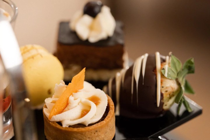 Assorted desserts including a chocolate-covered strawberry and a tart with cream on a black tray.