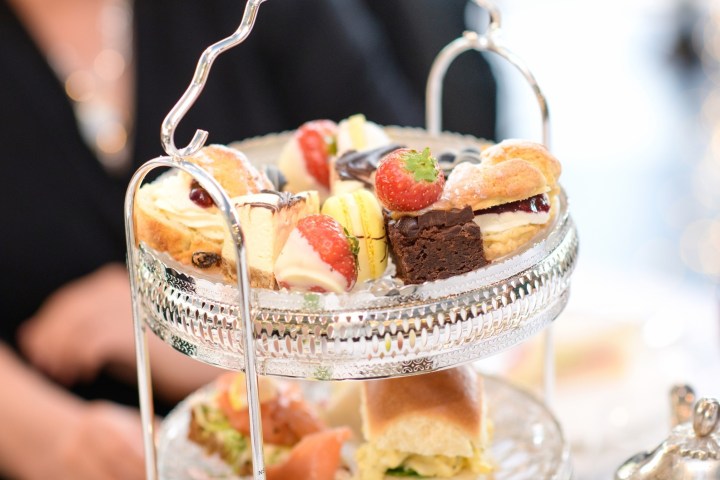 Tiered tray with assorted pastries and desserts, including strawberries and chocolate, in a dining setting.