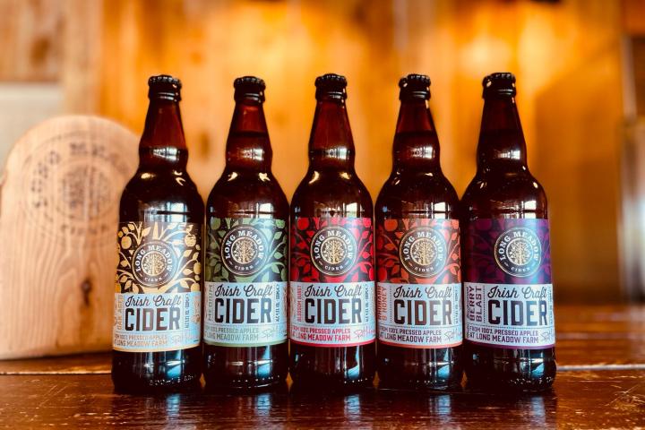 Five bottles of Irish Craft Cider on a wooden surface with varied labels.